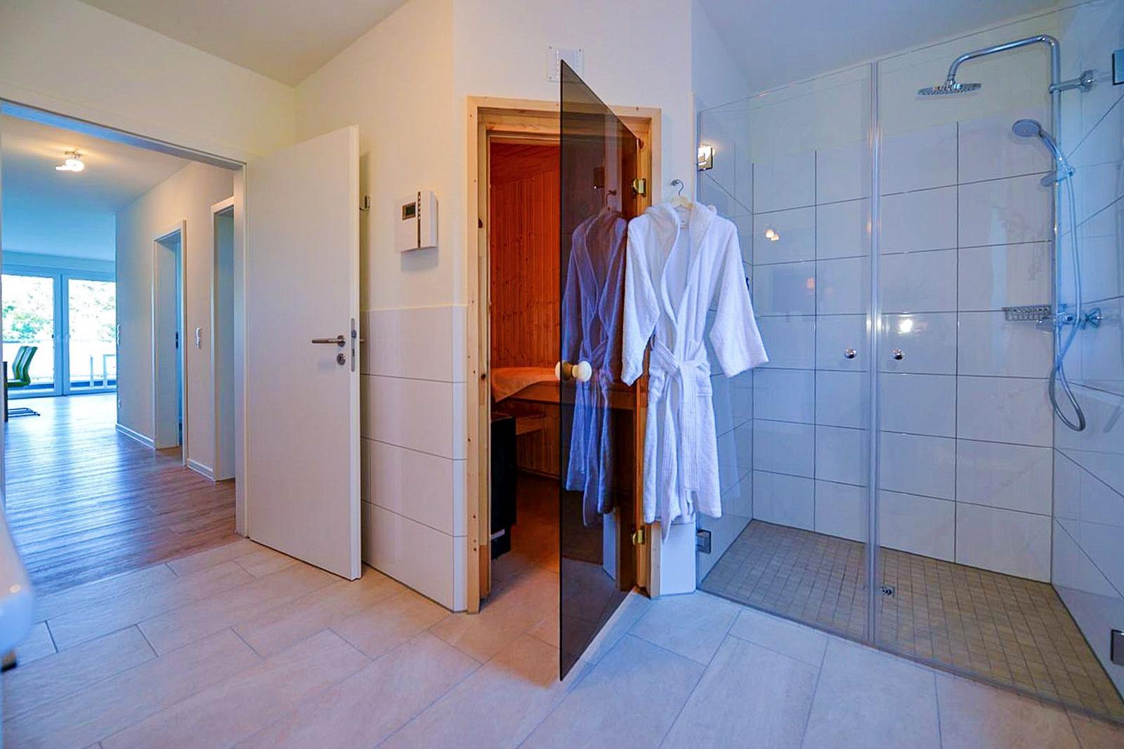 Dusche mit Glaswand, Sauna und Bademäntel hängen an der Tür.