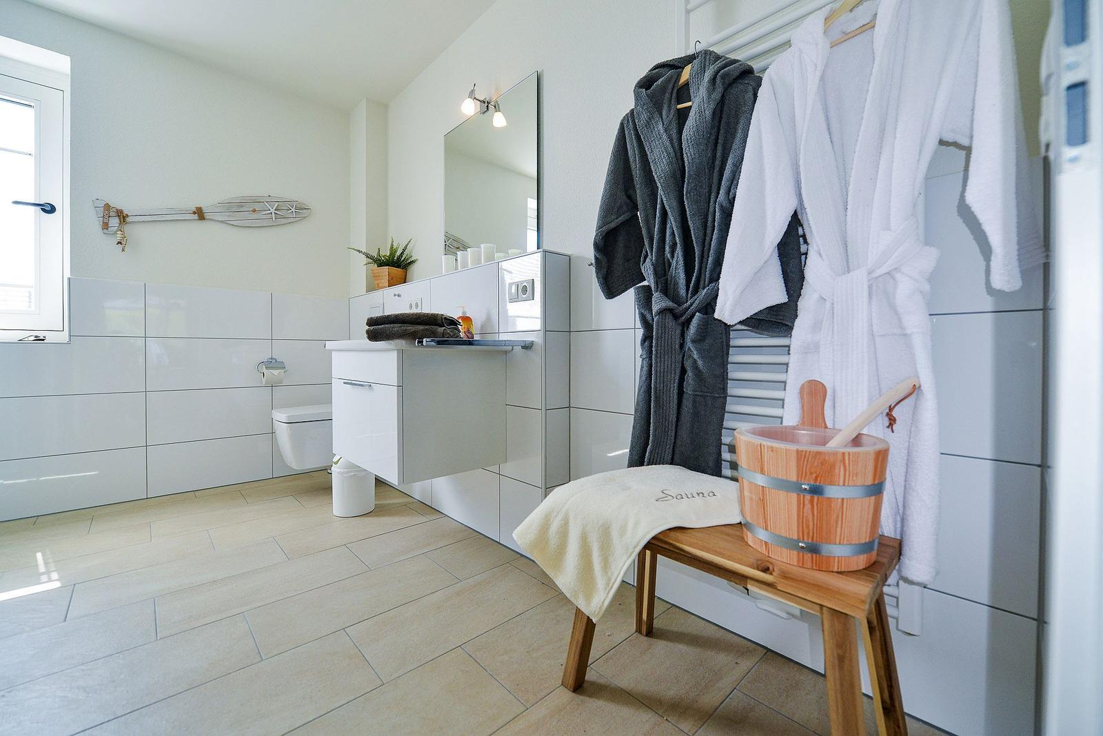 Badezimmer mit Dusche, Toilette und Waschbecken. Davor hängen Bademäntel und steht ein Holzwaschbecken.