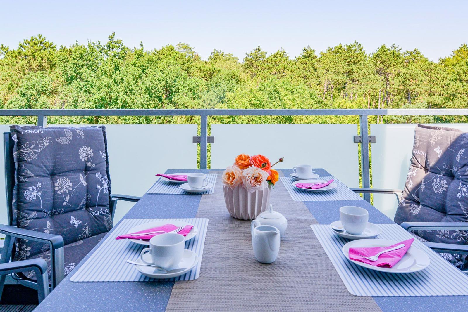 Terrasse mit Tisch, Stühlen und Blick auf Wald.