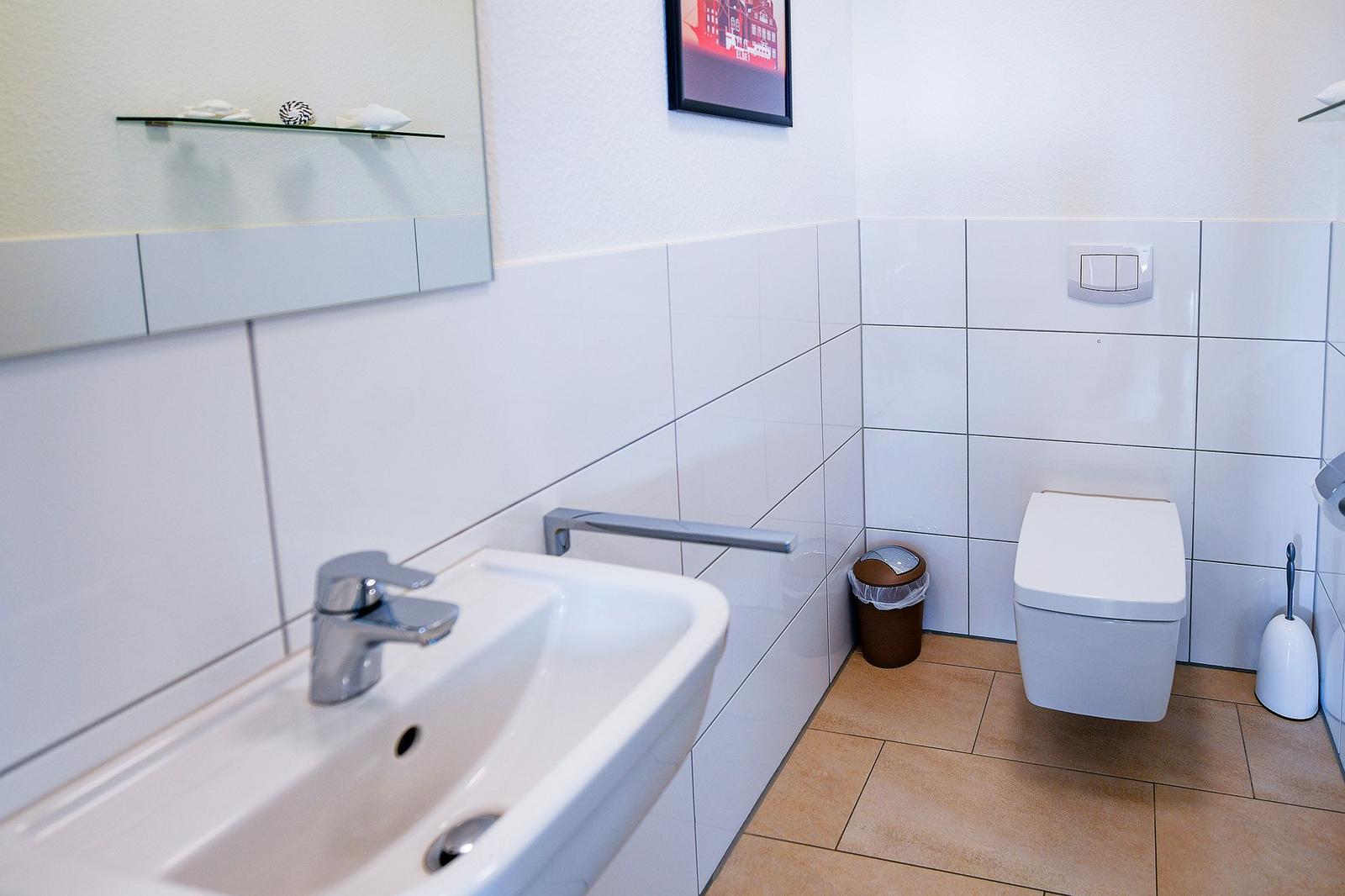 Bad mit Waschbecken, Spiegel, Toilette und Mosaikfliesen an den Wänden.