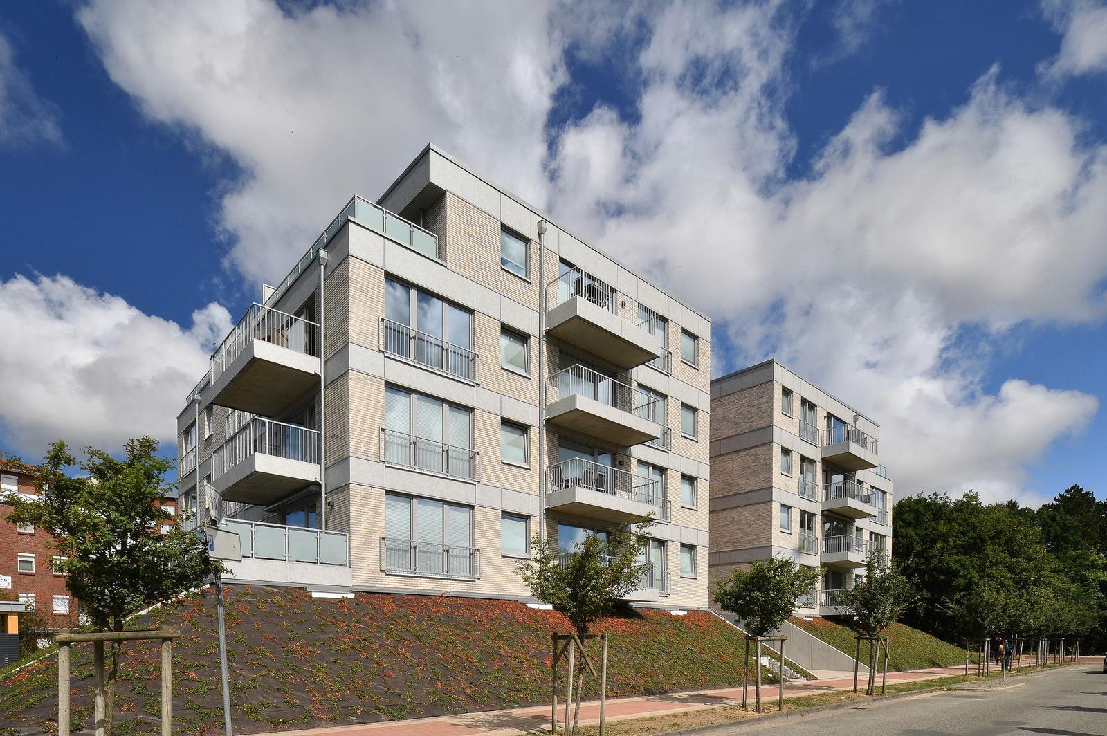 Moderne Wohngebäude mit Balkonen und begrünter Hangflanke unter blauem Himmel.