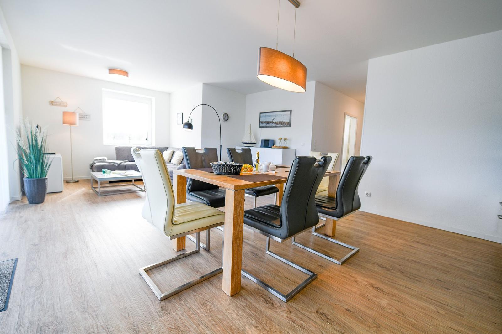 Esszimmer mit Holztisch und Stühlen, Wohnbereich mit Sofa und Fenster.