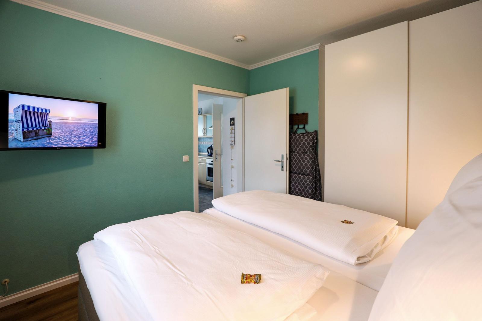 Schlafzimmer mit Bett, Fernseher und Tür zur Küche.