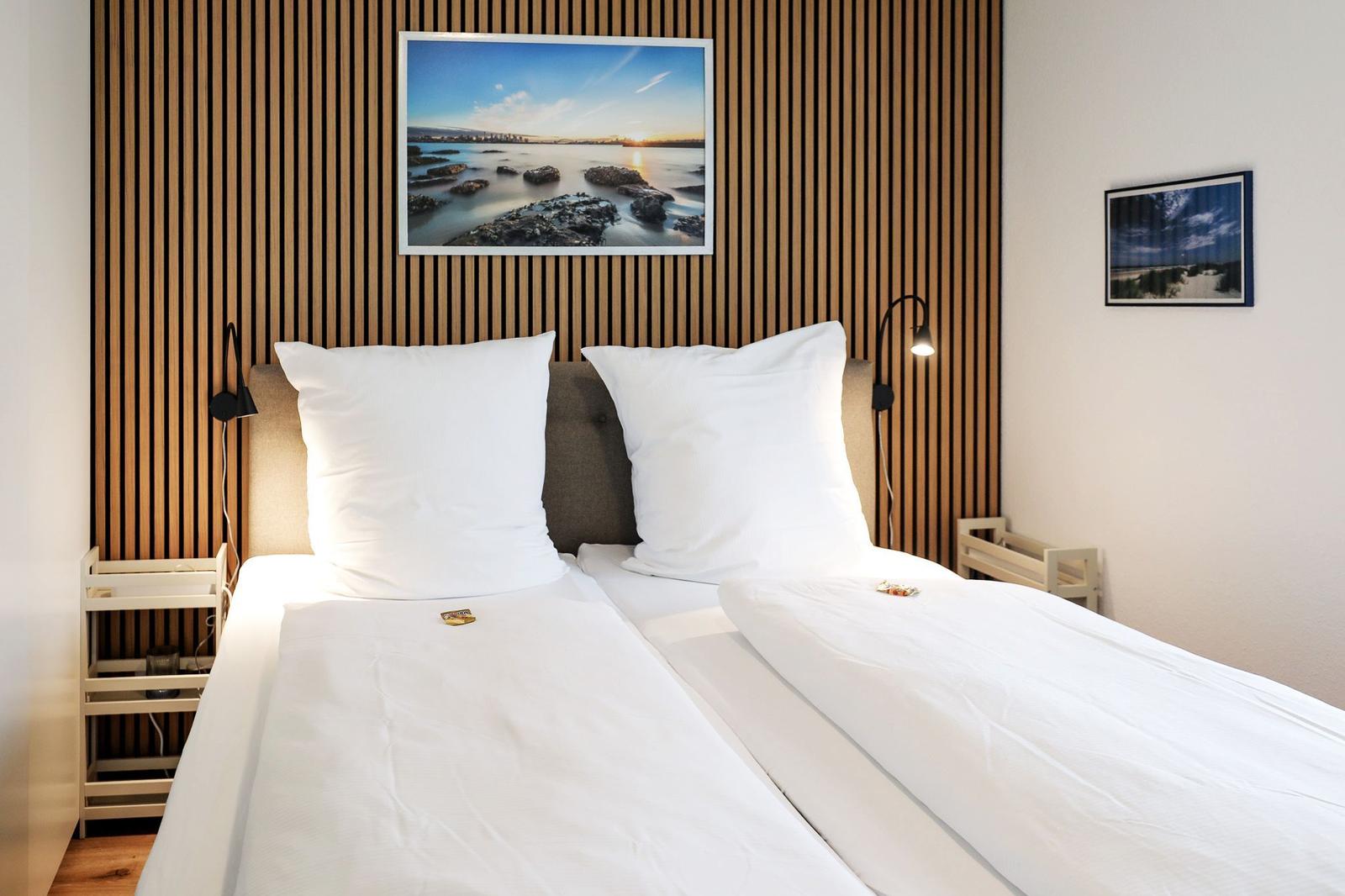 Zwei Betten mit weißen Bettwäsche, Holzwand und Wandbild.