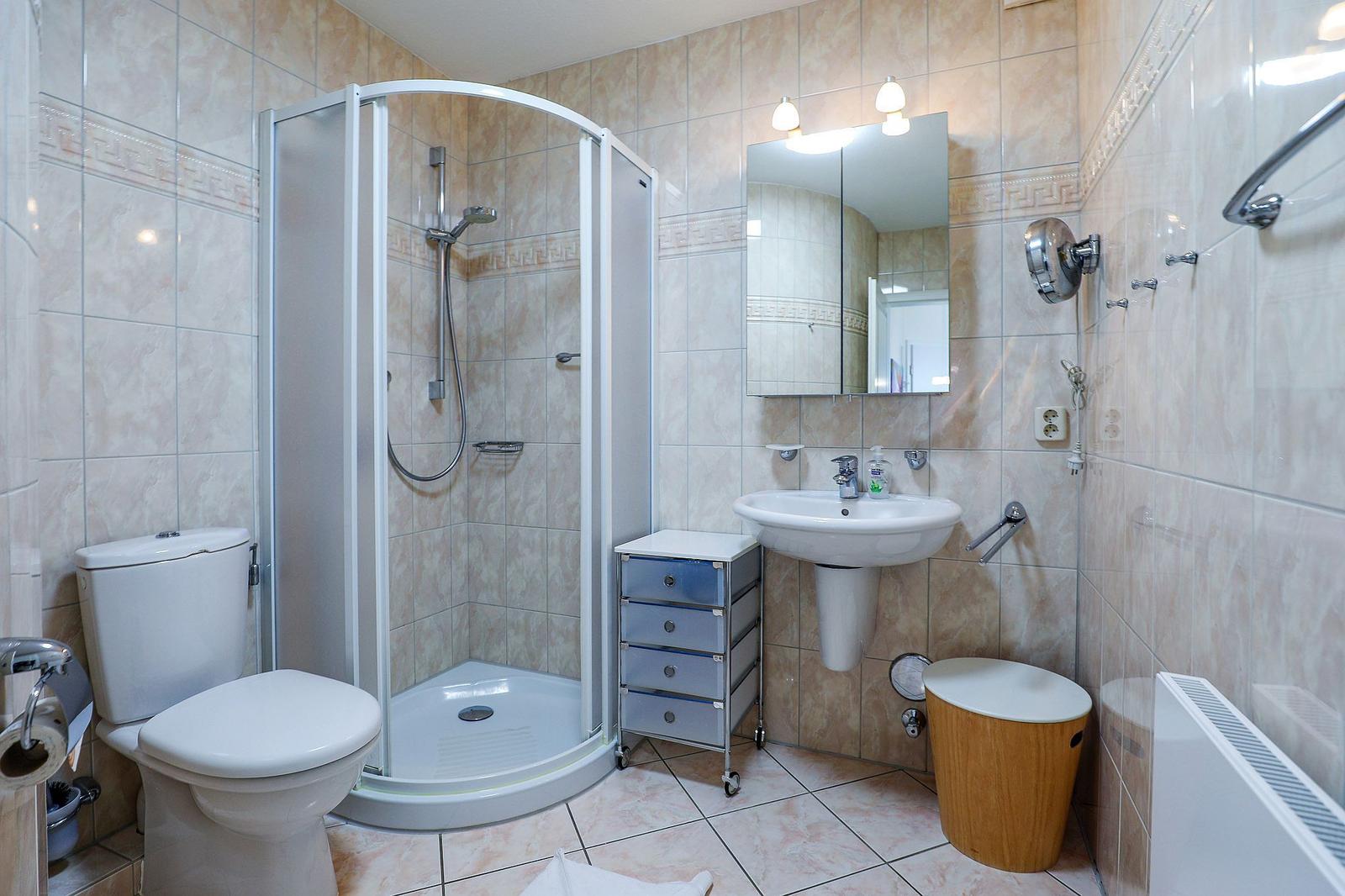 Bathroom with shower, sink, and toilet. Tiled walls and floor.