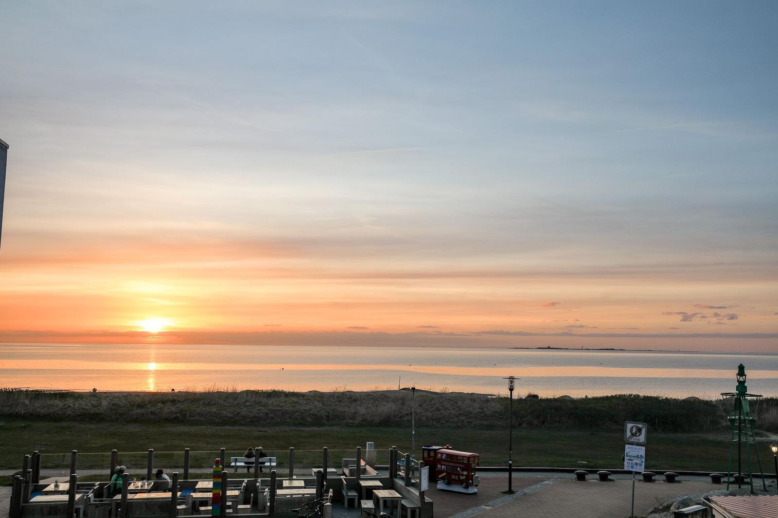 Sunset over the sea with beach area and seating.