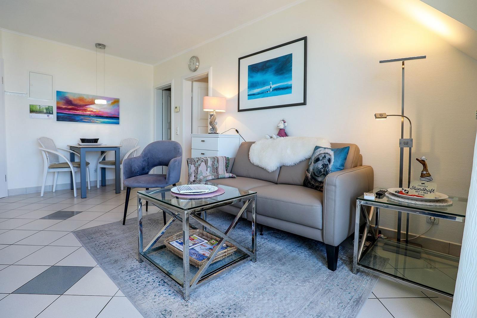 Living room with sofa, coffee table, and dining area. Wall art and floor lamp visible.