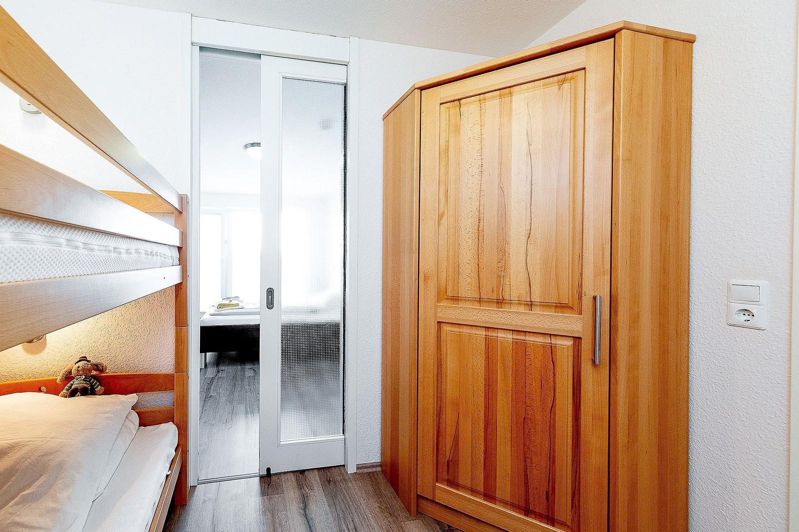 Schlafzimmer mit Doppelstockbett und Holzschrank. Durchgang zur Badezimmer.
