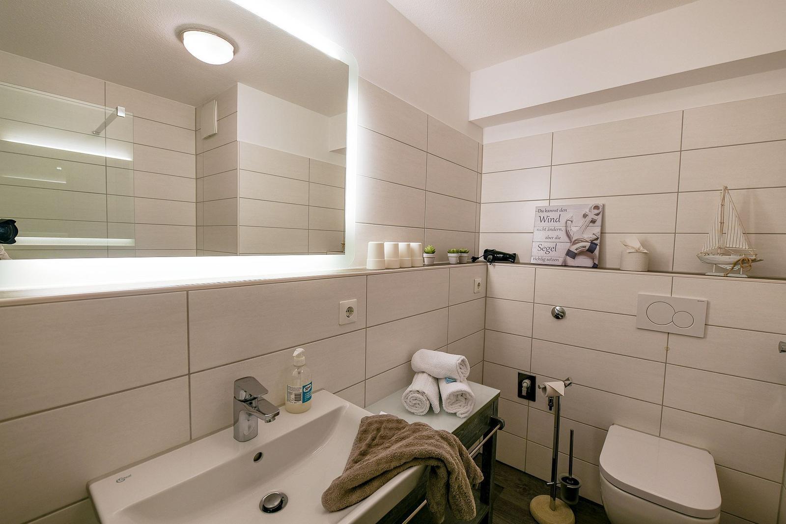 Badezimmer mit Waschbecken, Spiegel, Toilette und Handtüchern.
