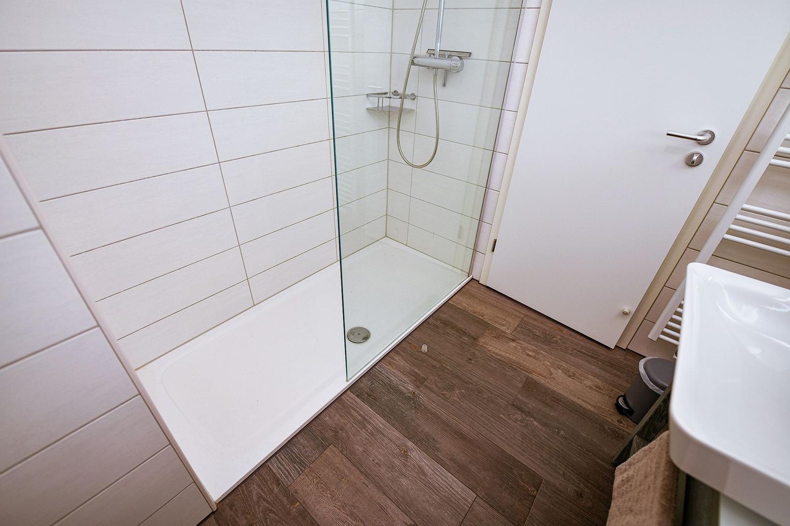 Bad mit Dusche, Waschbecken und Holzboden.