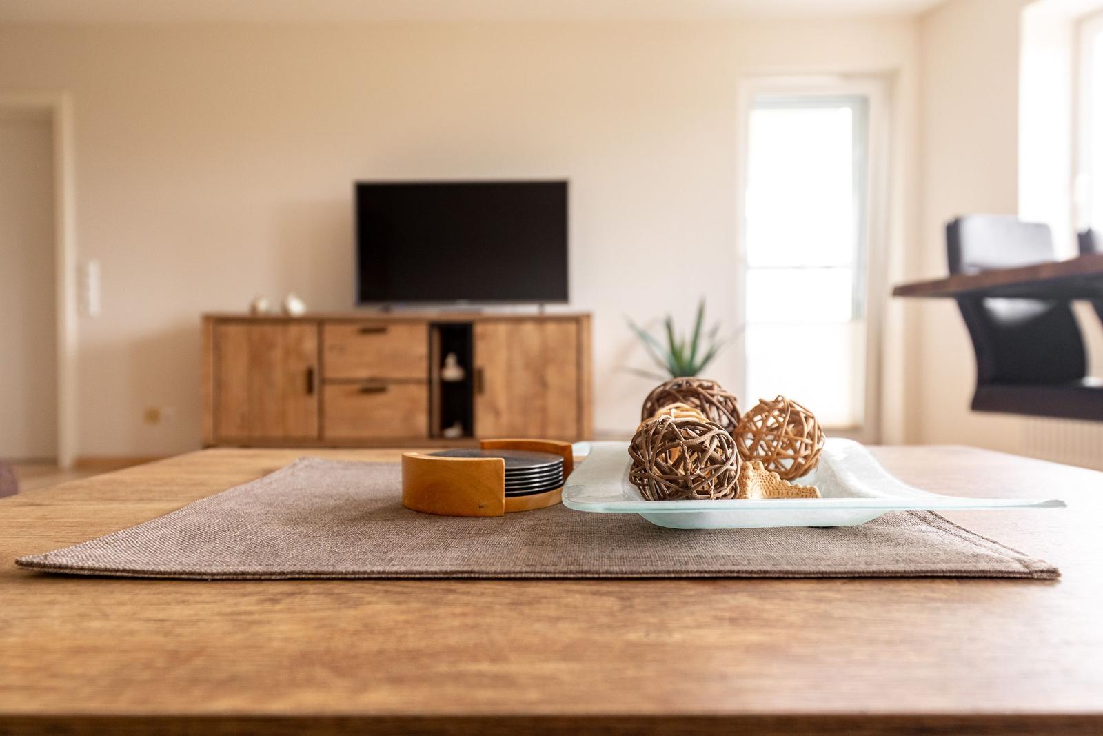 Holztisch mit Untersetzer und Dekoration im Wohnzimmer mit Fernseher und Holzschrank.