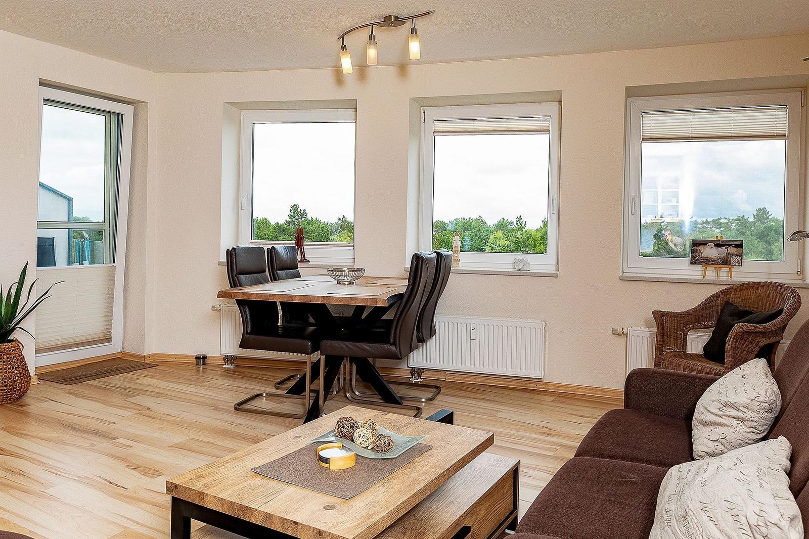 Wohn- und Essbereich mit Holzboden, Fenstern und moderner Einrichtung.