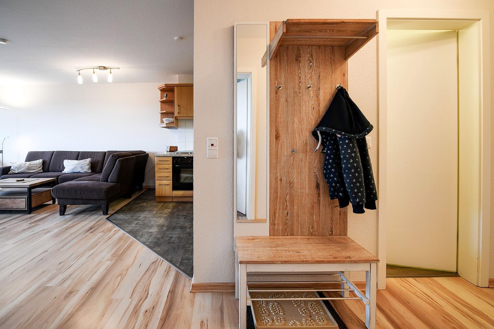 Eingangsbereich mit Holzgarderobe und Spiegel. Im Hintergrund Wohn- und Küchenbereich.