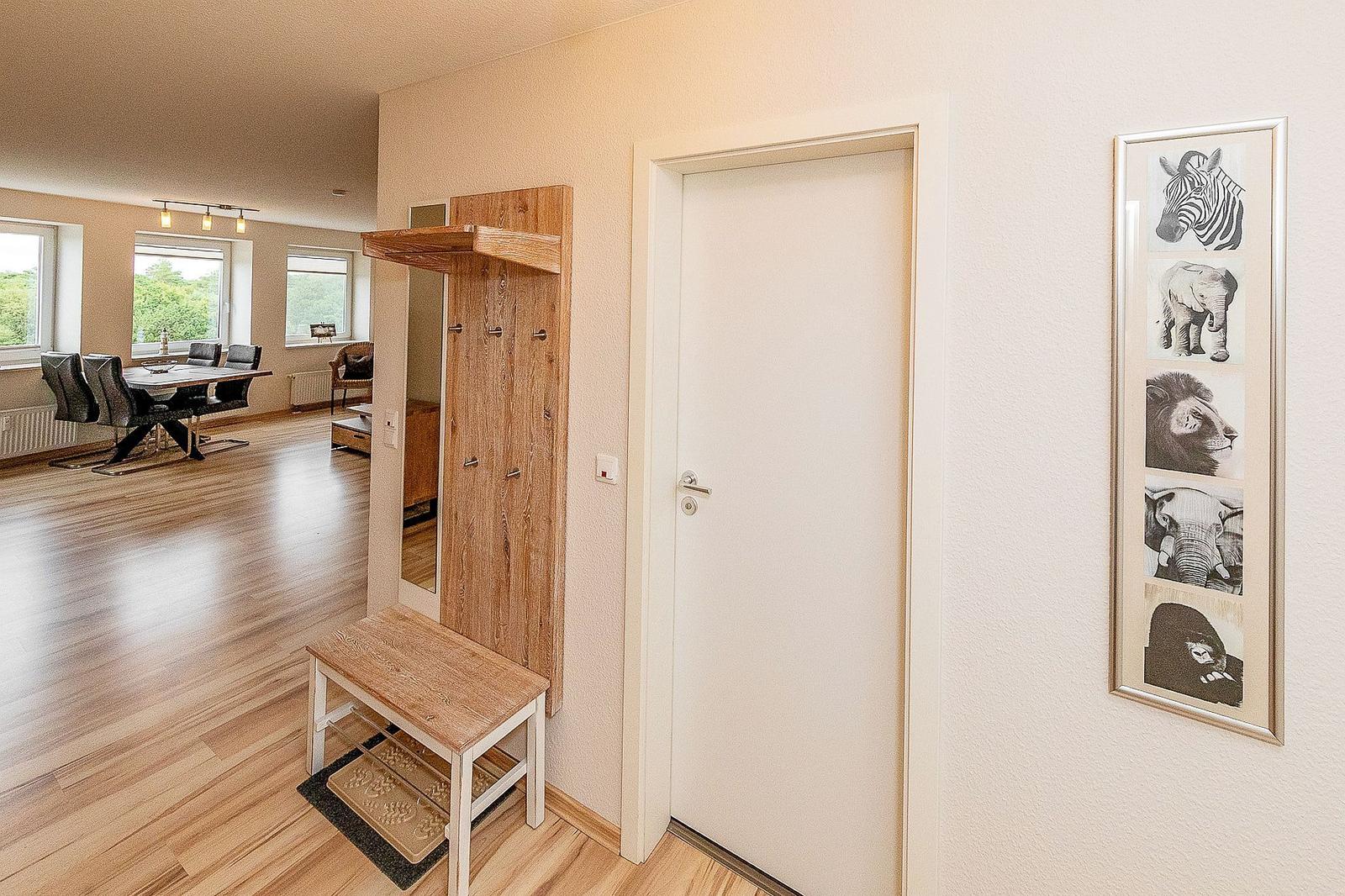 Eingangsbereich mit Holzgarderobe, Stuhl und Wandbild mit Tieren. Im Hintergrund Esszimmer mit Tisch und Stühlen.