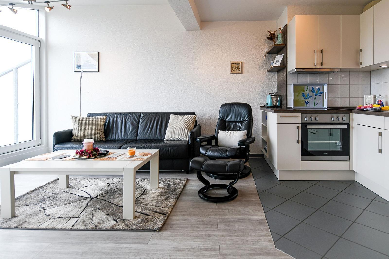 Wohnbereich mit Sofa, Sessel und Küchenzeile.