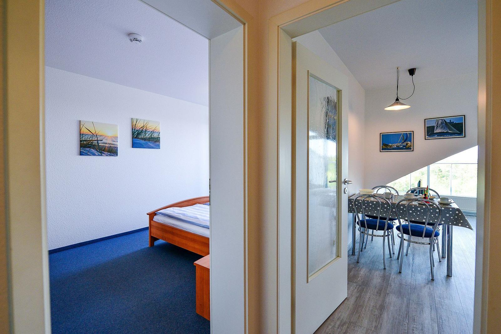 Schlafzimmer mit Bett und Wandbildern. Nebenraum mit Esstisch und Stühlen.