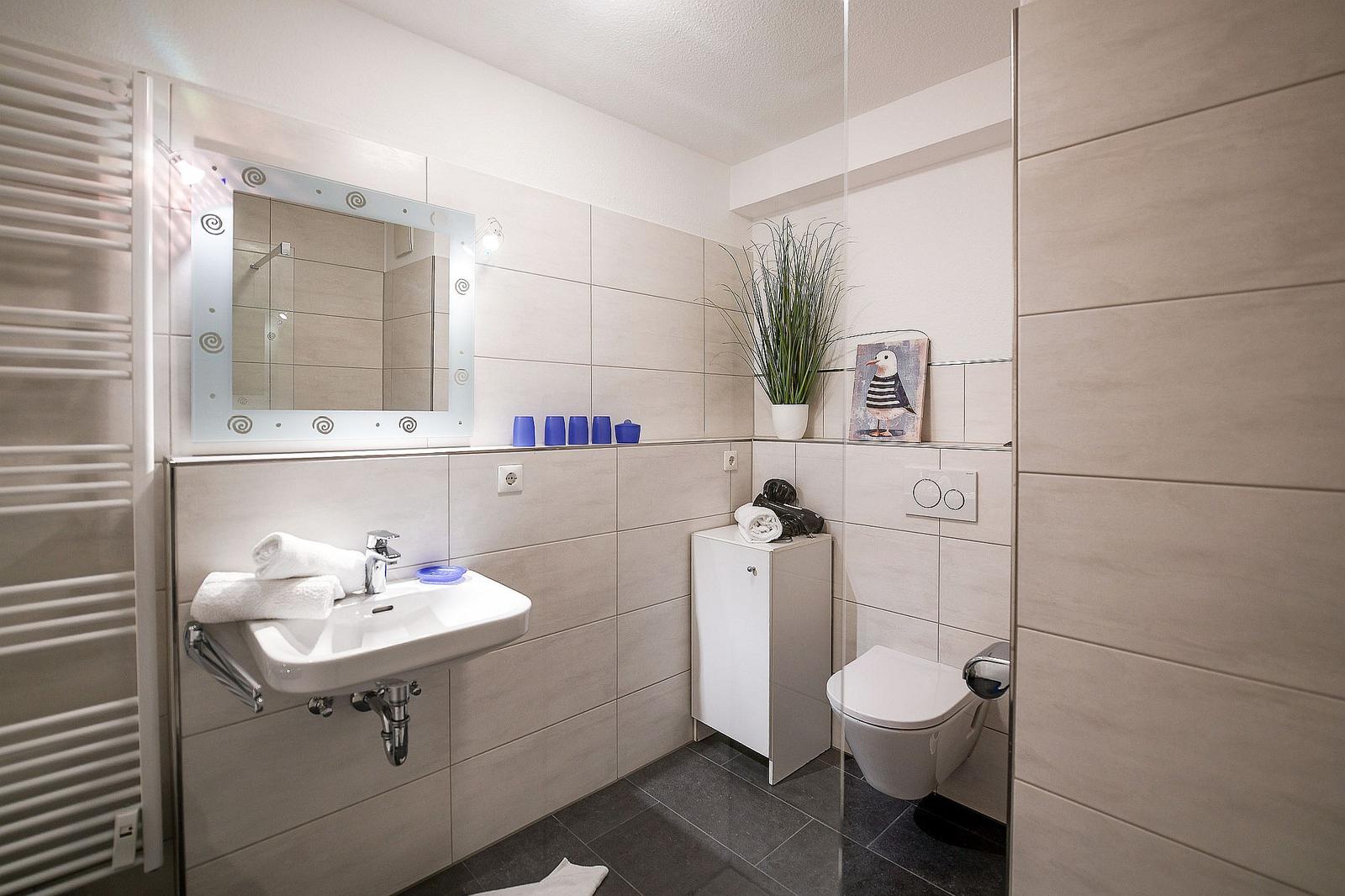Badezimmer mit Waschbecken, Spiegel, Toilette und Dusche.