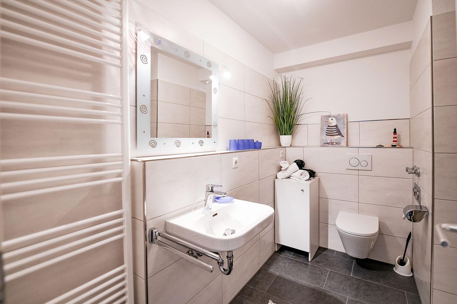 Badezimmer mit Waschbecken, Spiegel, Toilette und Heizung.