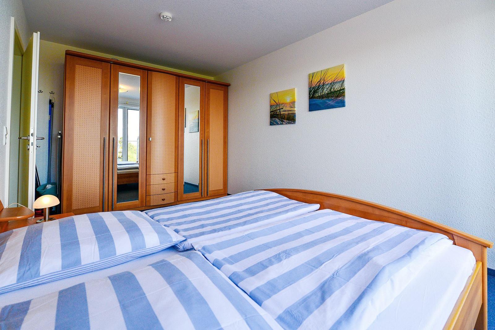 Schlafzimmer mit Doppelbett, Kleiderschrank und Wandbildern.
