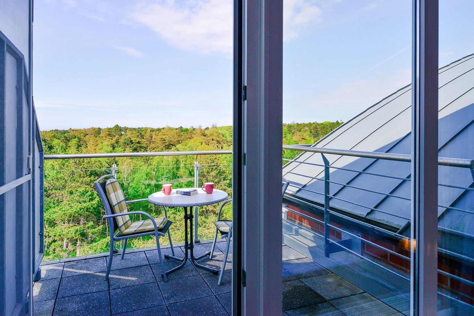 Balcony with table and chairs overlooking a forested area.