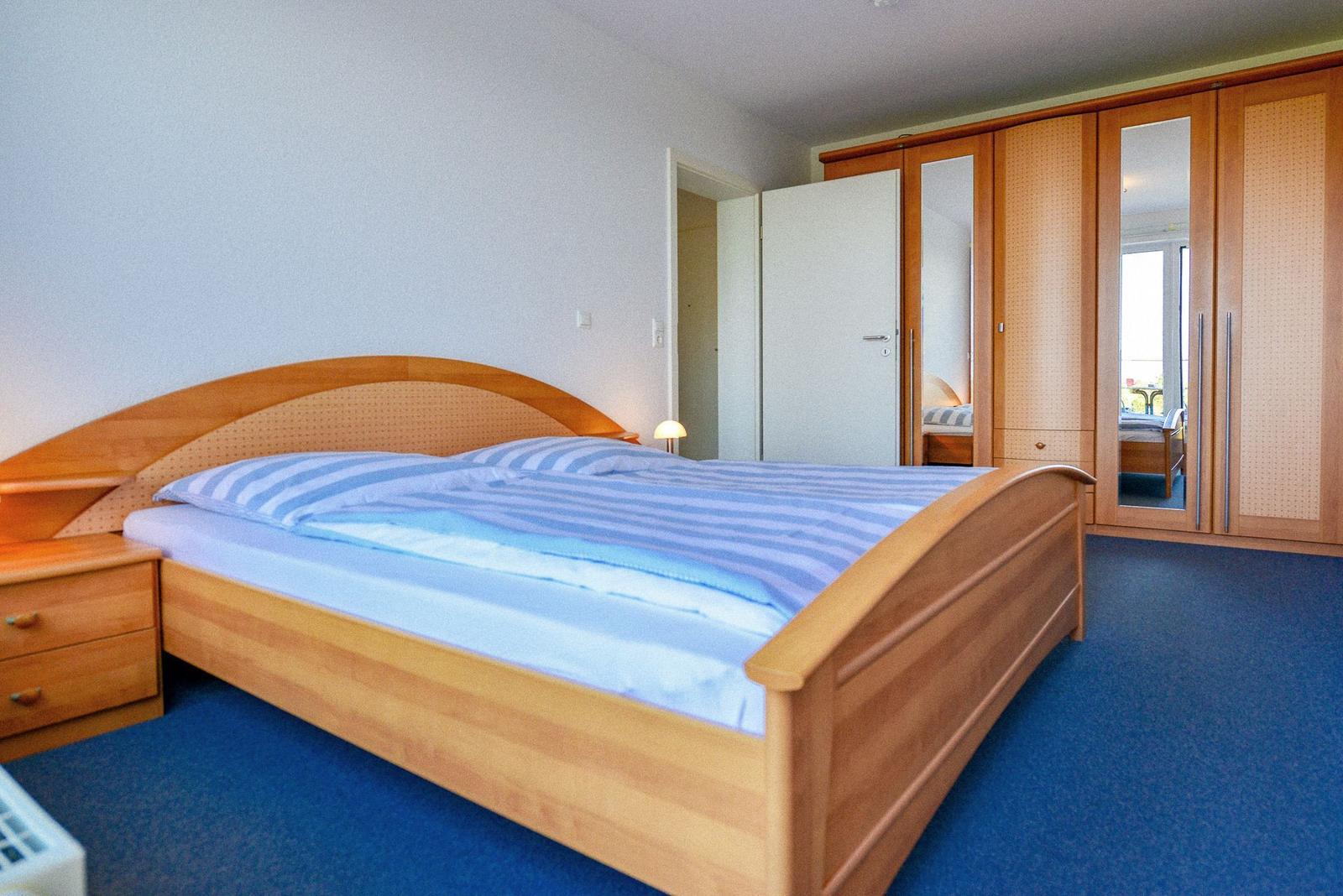 Schlafzimmer mit Holzbett, Schrank und blauem Teppichboden.
