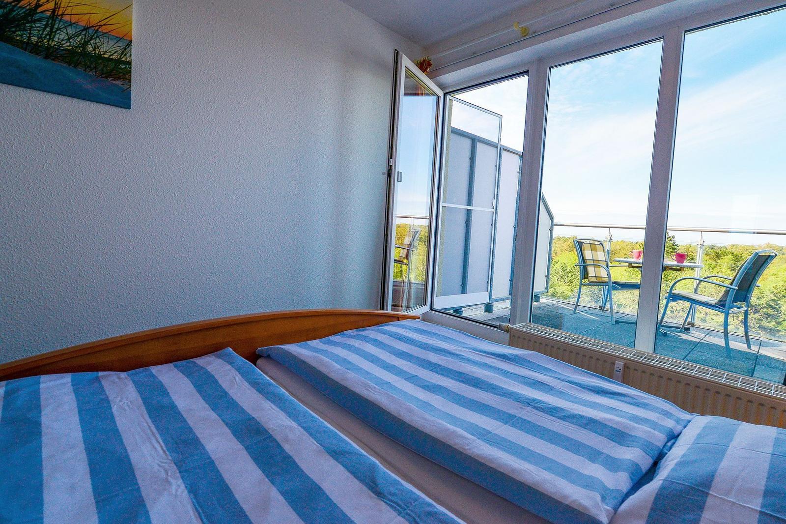 Zimmer mit Balkon und blau-weißem Bettbezug. Blick auf grüne Landschaft.