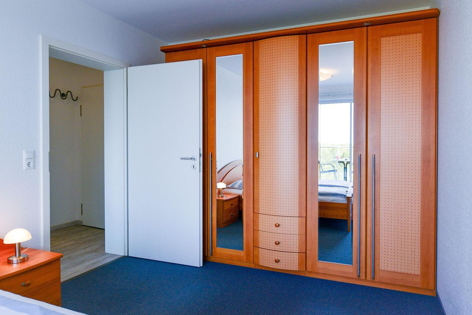 Schlafzimmer mit Holzschrank, Spiegeltüren und blauem Teppichboden.