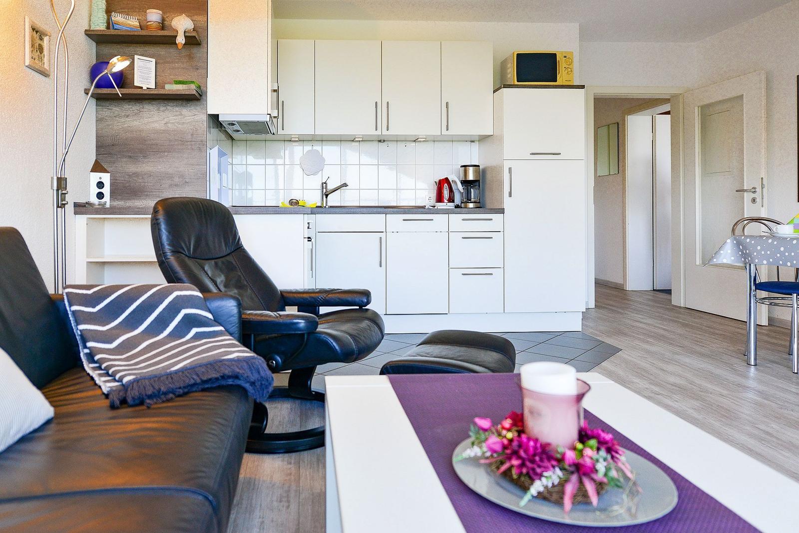Wohnbereich mit Küche, Sofa, Sessel und Esstisch. Weiße Küchenmöbel und Holzboden.