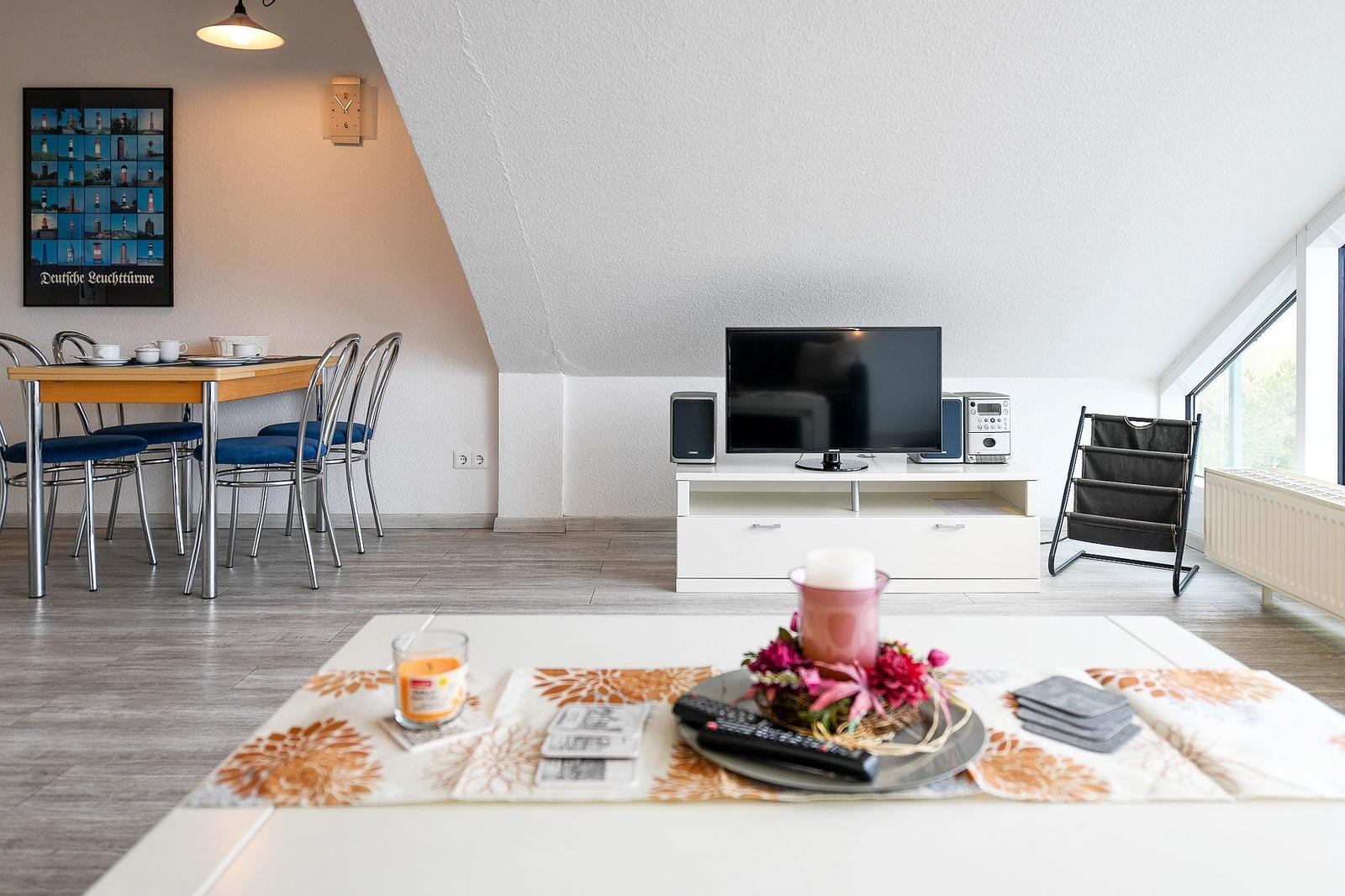Wohn- und Essbereich mit TV, Tisch und Stühlen, Fenster und Dachschräge.