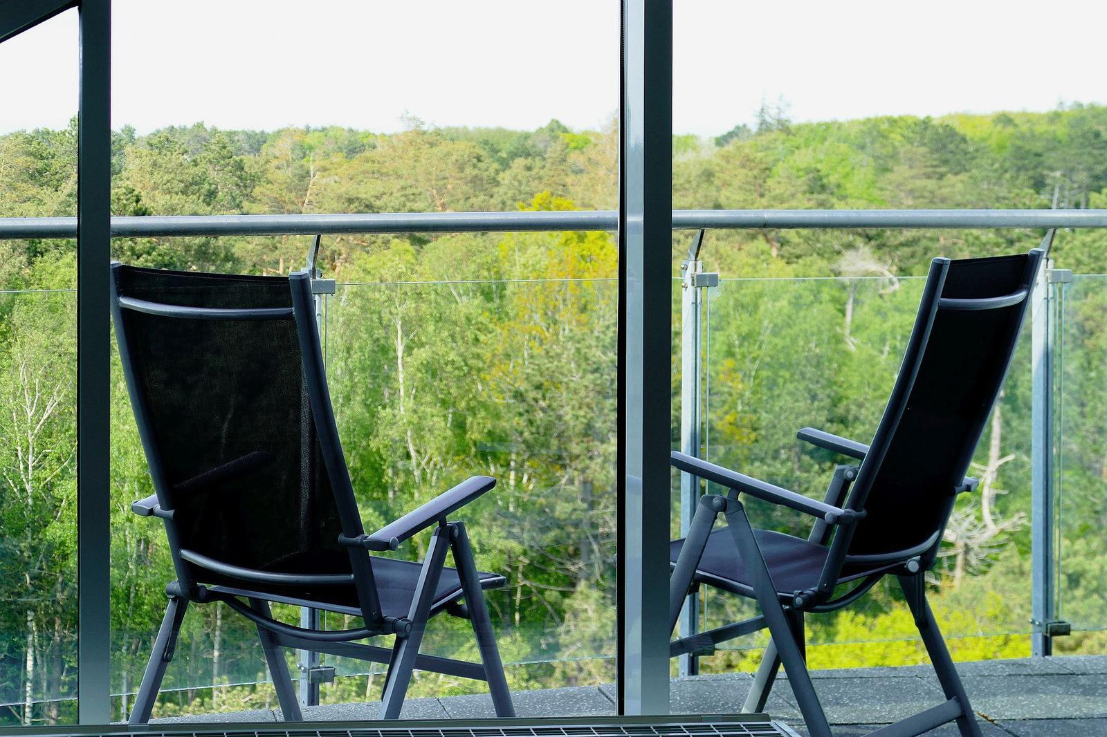 Zwei schwarze Liegestühle auf einer Terrasse mit Blick auf einen Wald.