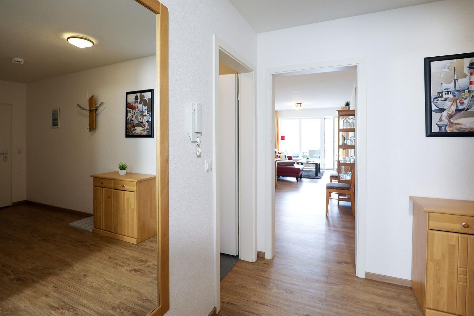 Eingangsbereich mit Holzschrank und Spiegel. Durchgang in Wohn- und Essbereich mit Möbeln.