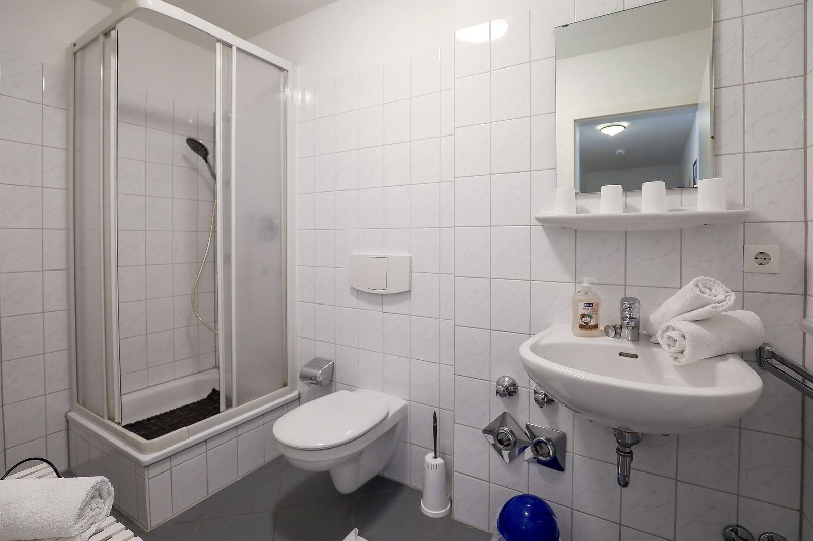 Badezimmer mit Dusche, Toilette und Waschbecken mit Spiegel und Handtüchern.