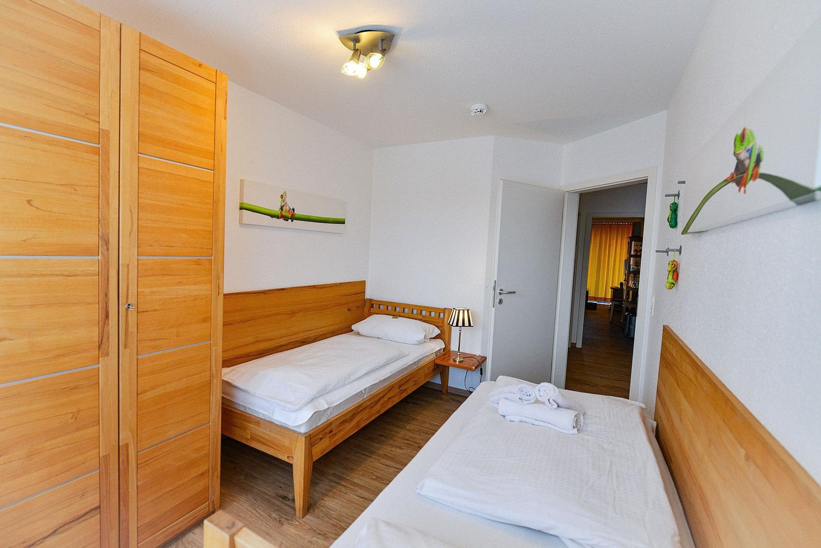 Zwei Einzelbetten, Holzmöbel und Wandbilder mit Froschmotiven.