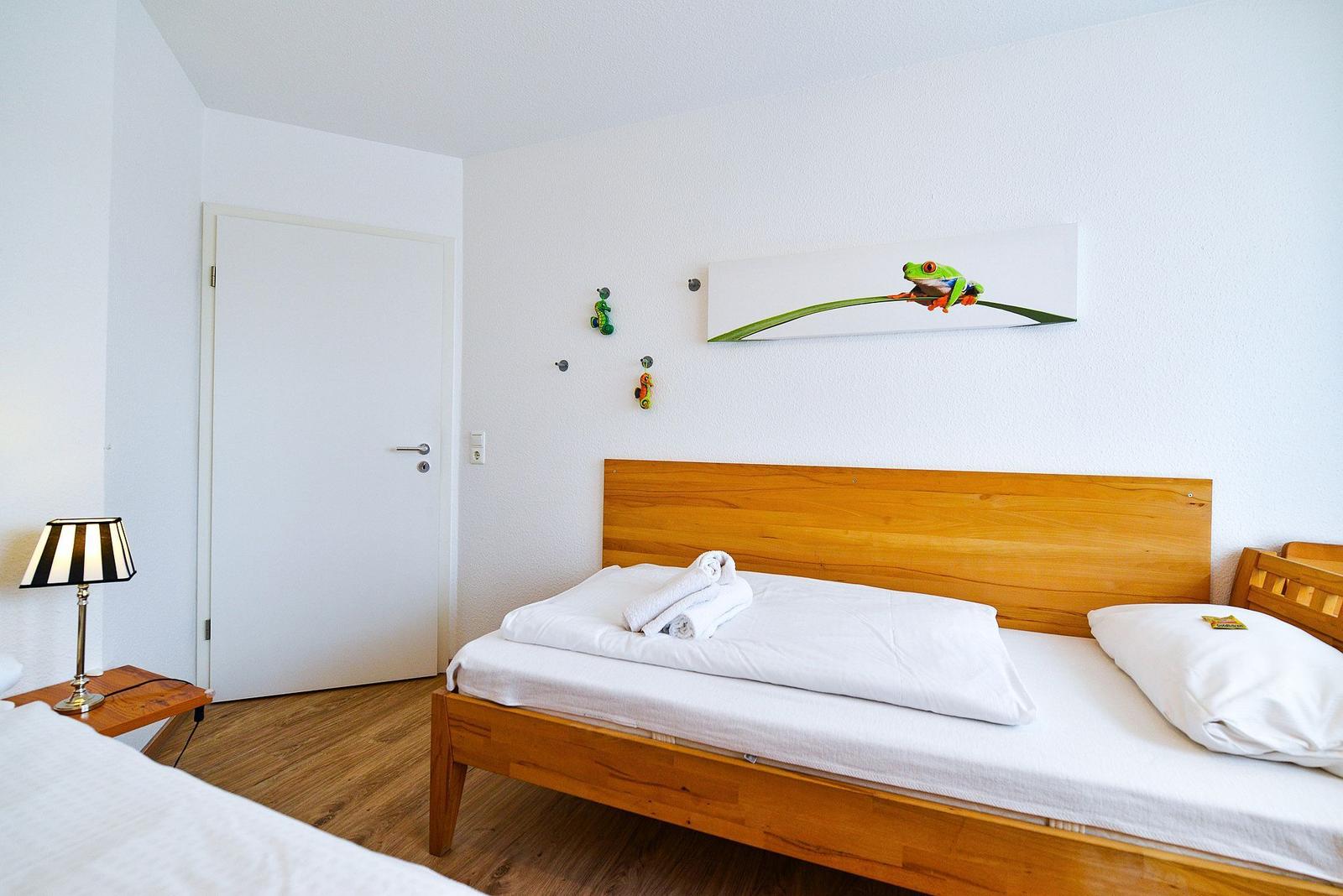 Schlafzimmer mit Holzbett, Wandbild mit Frosch und Nachttisch mit Lampe.