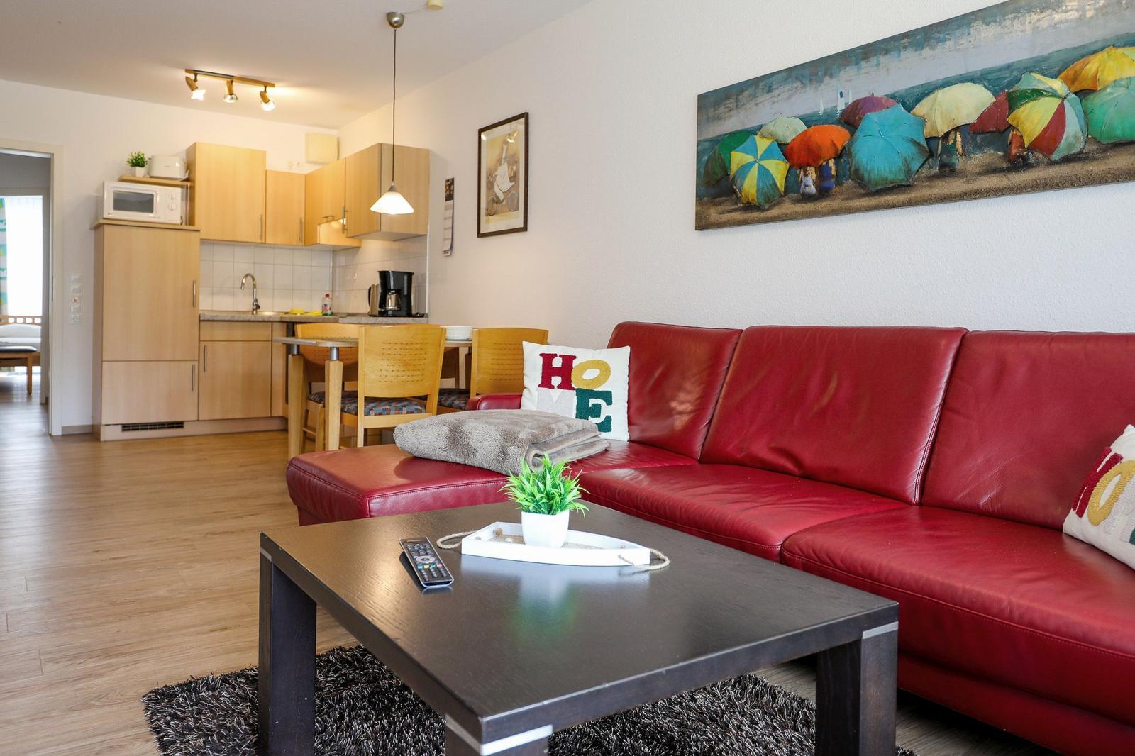 Ein Wohnzimmer mit rotem Sofa, Küchenbereich und Wandbild mit Regenschirmen.