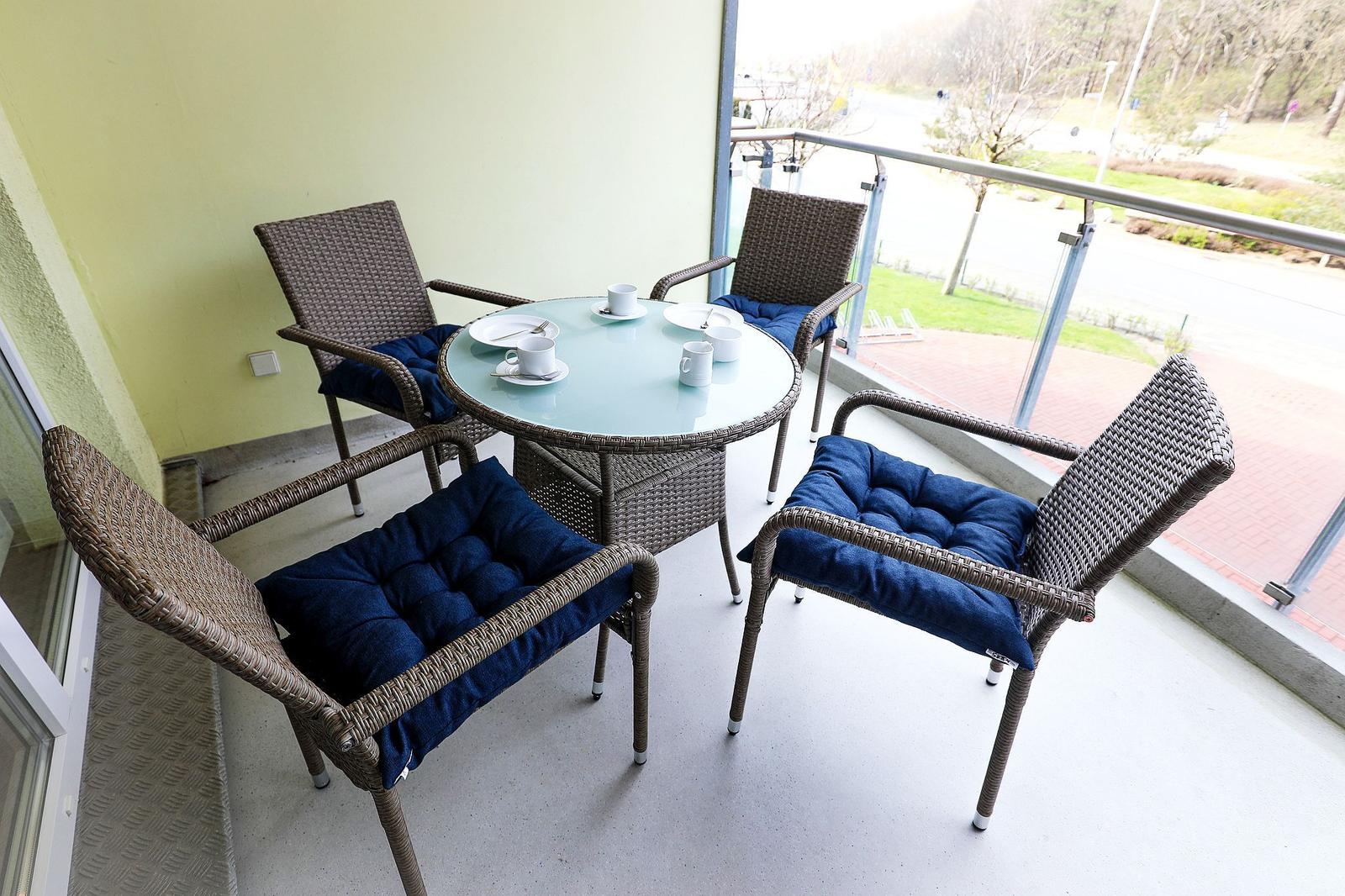 Balkon mit runden Tisch und vier Stühlen mit blauen Sitzkissen.