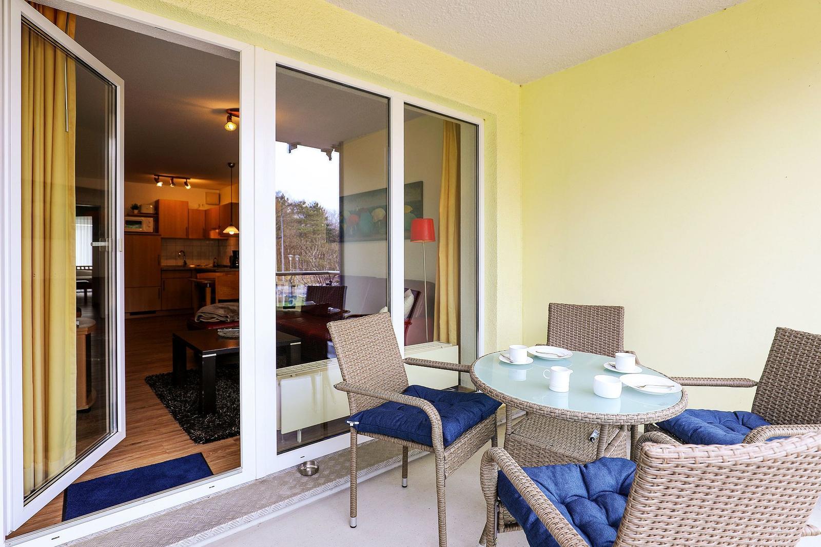 Terrasse mit Rattanmöbeln und Tisch. Durchgehendes Glas führt in die Wohnung.