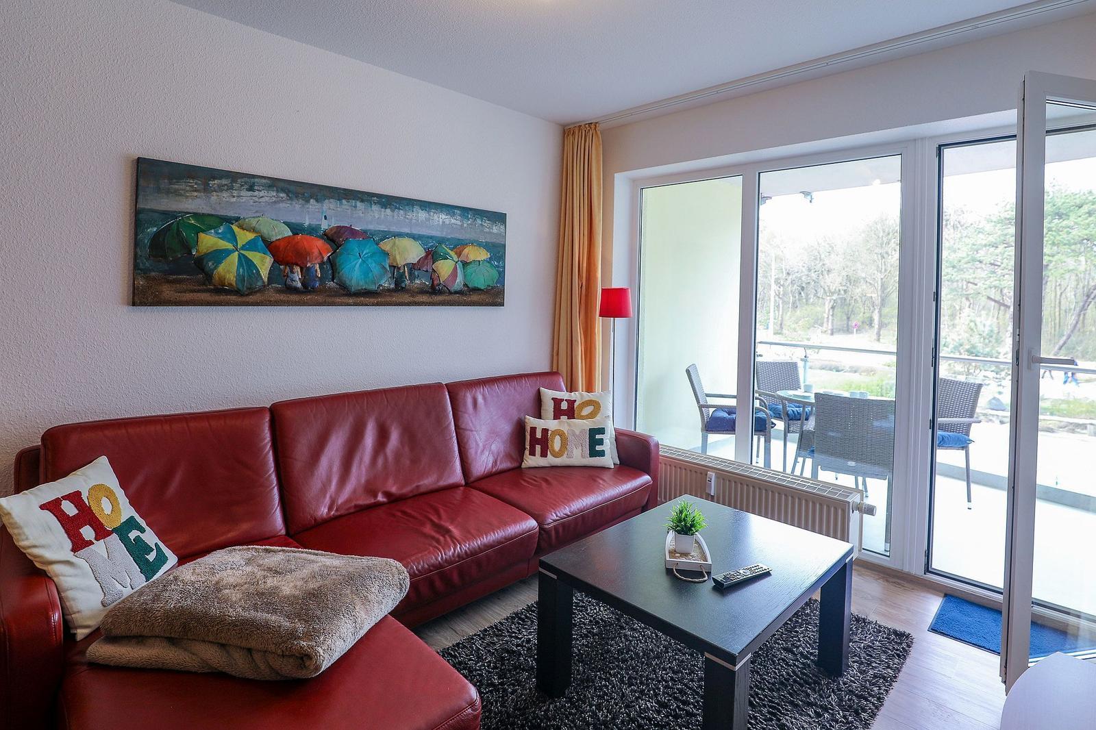 Ein Wohnzimmer mit rotem Sofa, Kissen und einer großen Glasfront zur Terrasse.