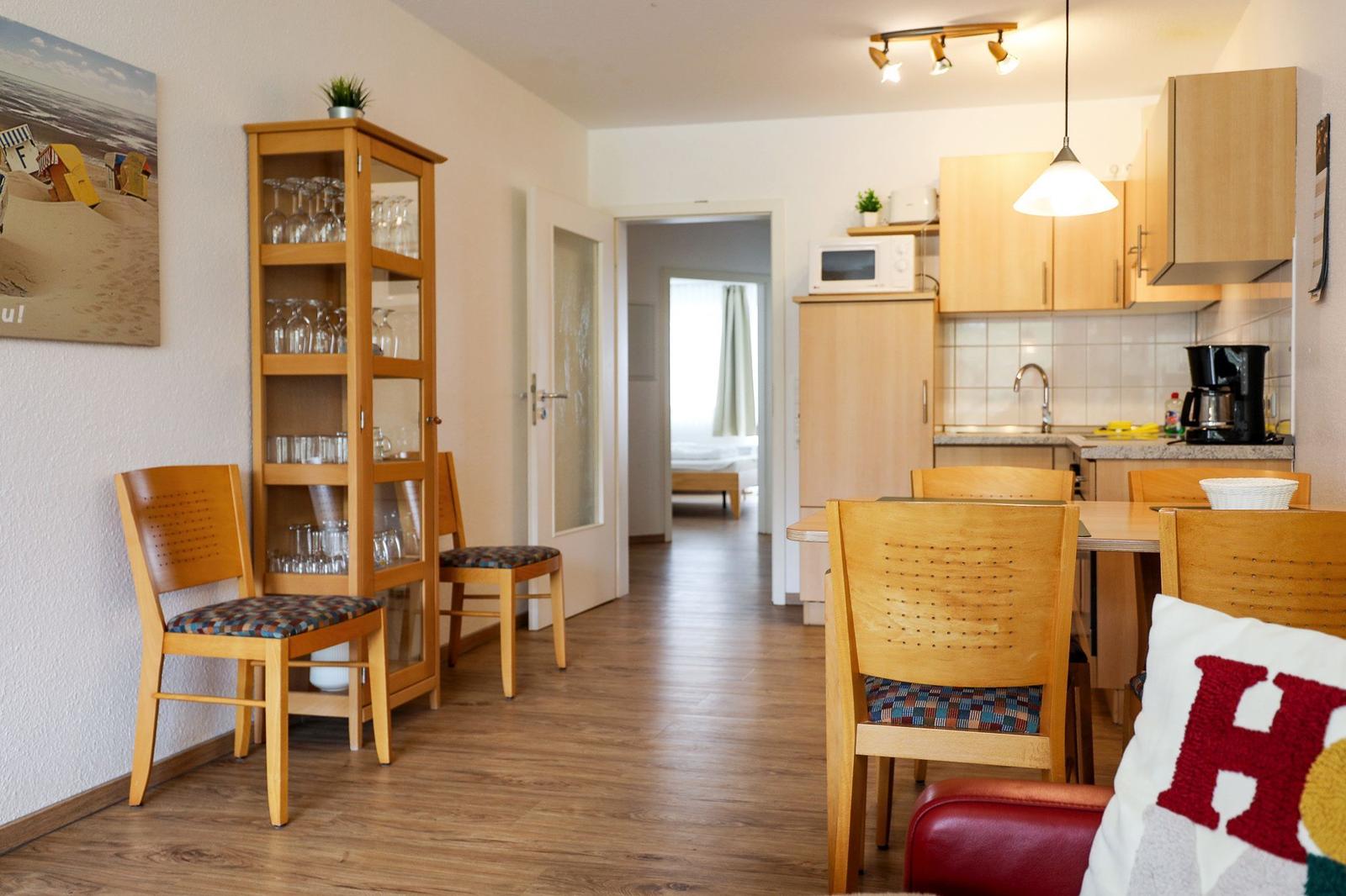 Küche und Essbereich mit Holzmöbeln und Glasregal. Blick in Schlafzimmer.