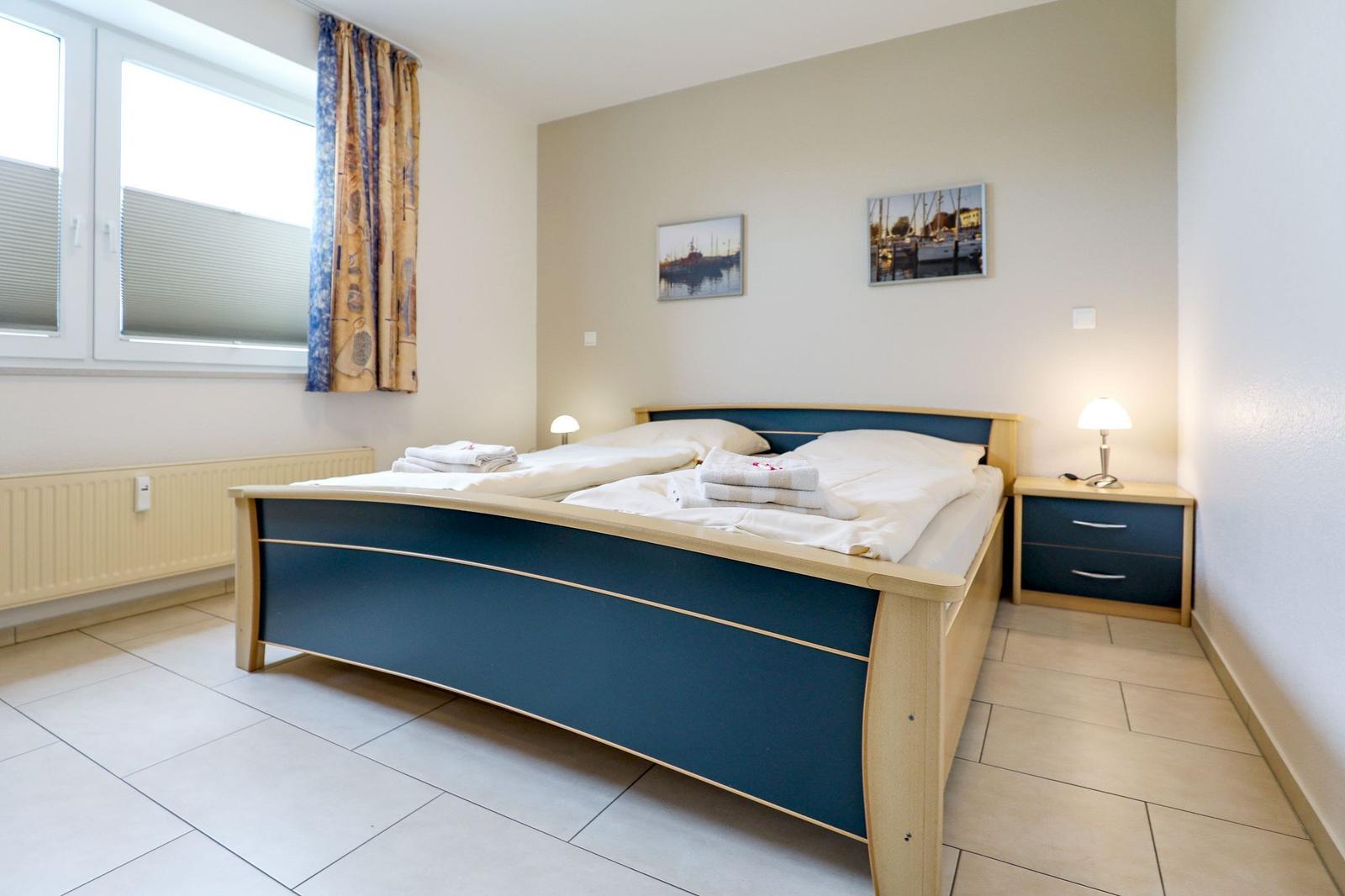 Schlafzimmer mit Doppelbett, Nachttisch und Fenster mit Vorhängen.