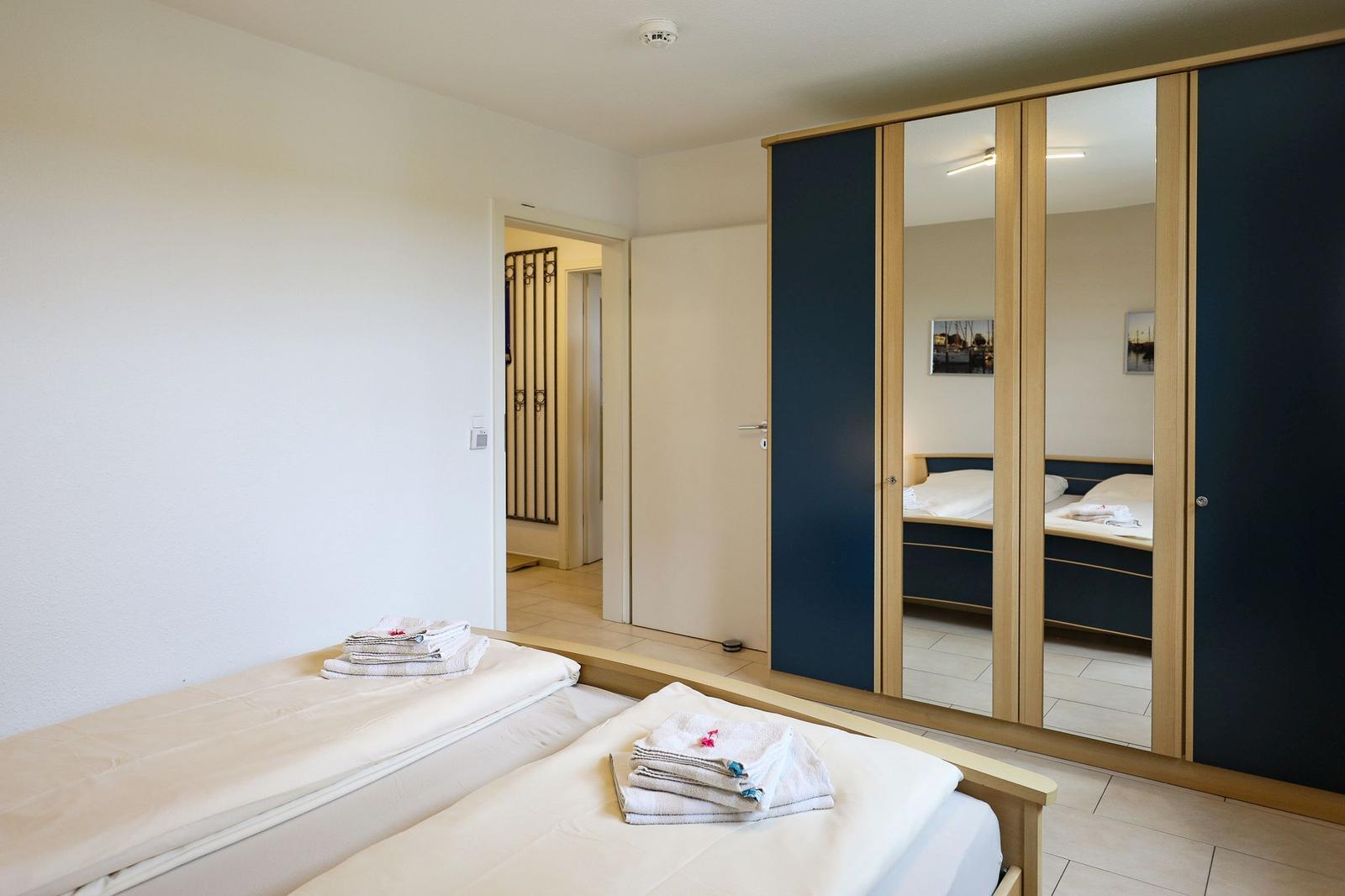 Zwei Betten mit Handtüchern, Spiegelschrank und Tür zum Flur.