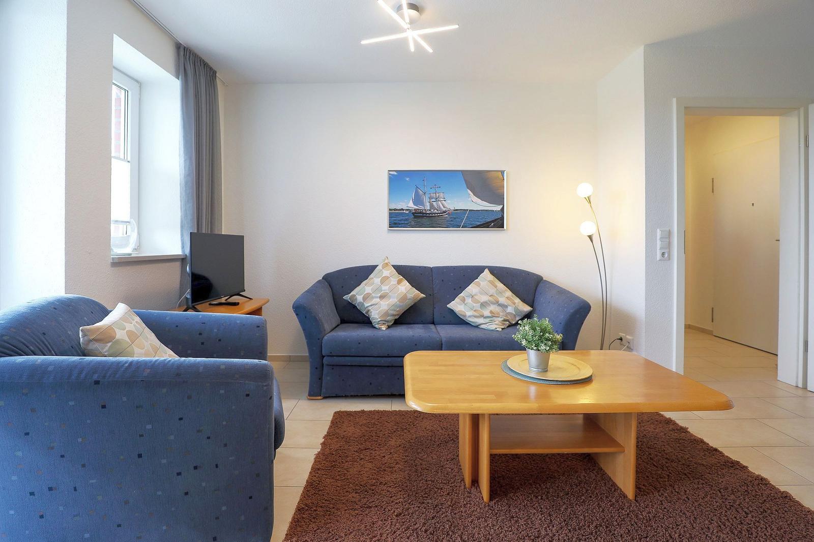 Wohnzimmer mit blauem Sofa, Holztisch und Wandbild mit Segelyacht.