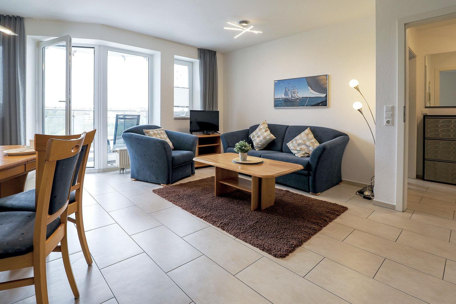 Wohnzimmer mit Sofa, Sessel, Couchtisch und Balkontür.