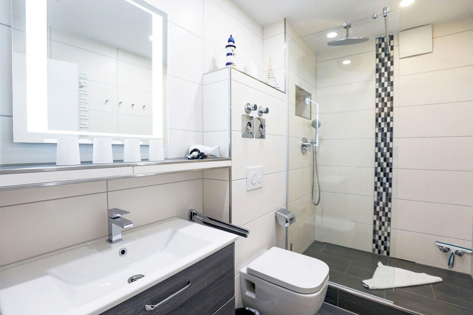 Badezimmer mit Dusche, Waschbecken und Toilette. Fliesen und Spiegel sind sichtbar.