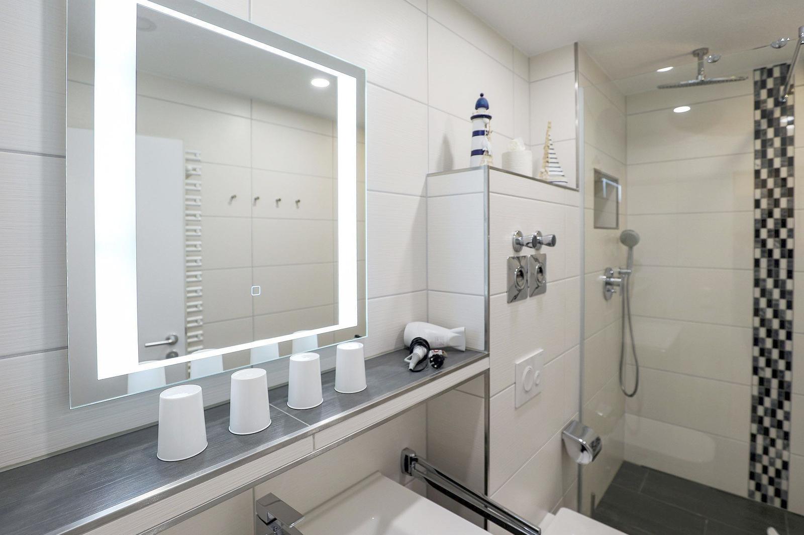 Badezimmer mit beleuchtetem Spiegel, Dusche und Waschbecken