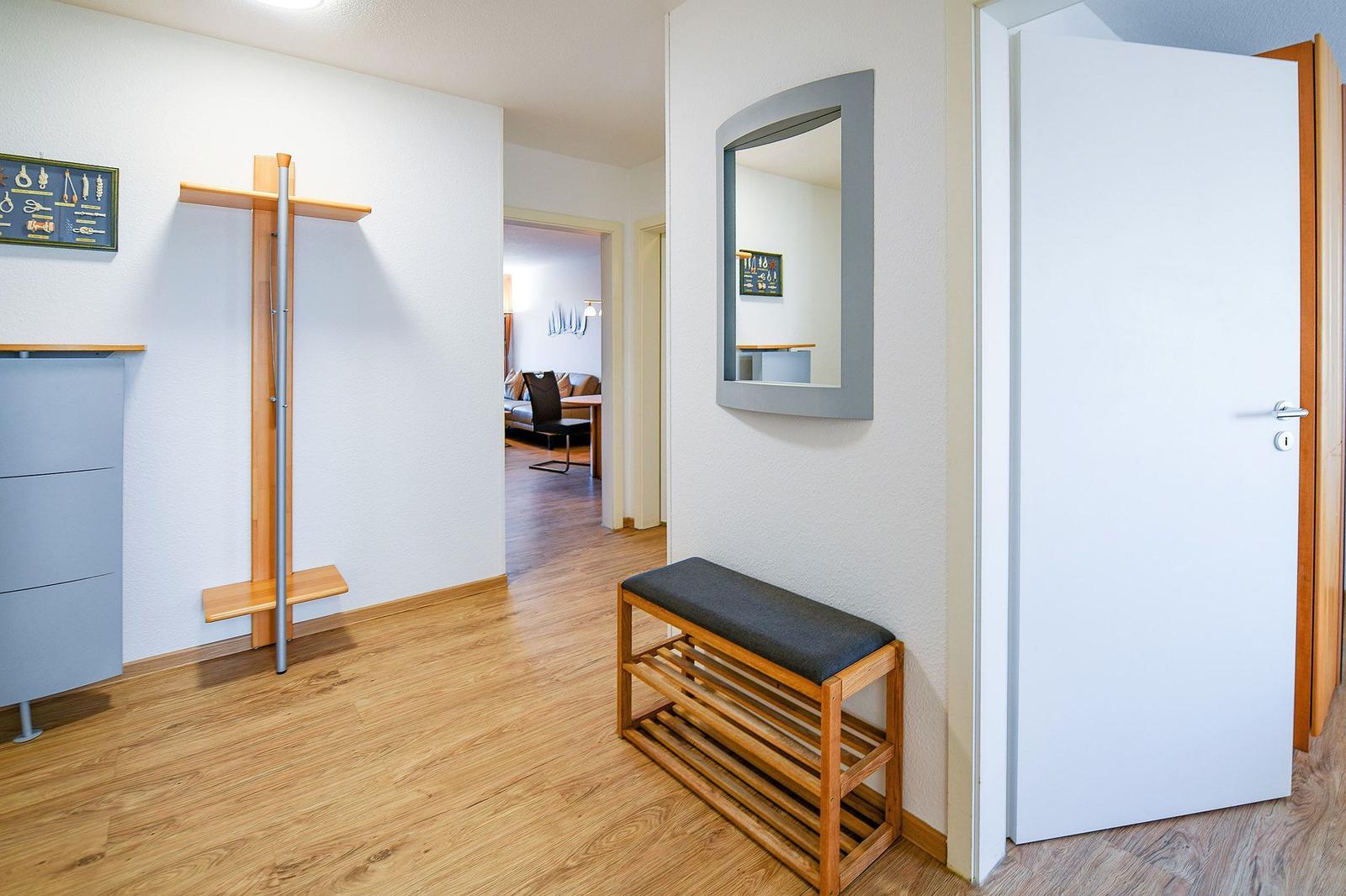 Eingangsbereich mit Spiegel, Bank und Garderobe. Durchgang ins Wohnzimmer.