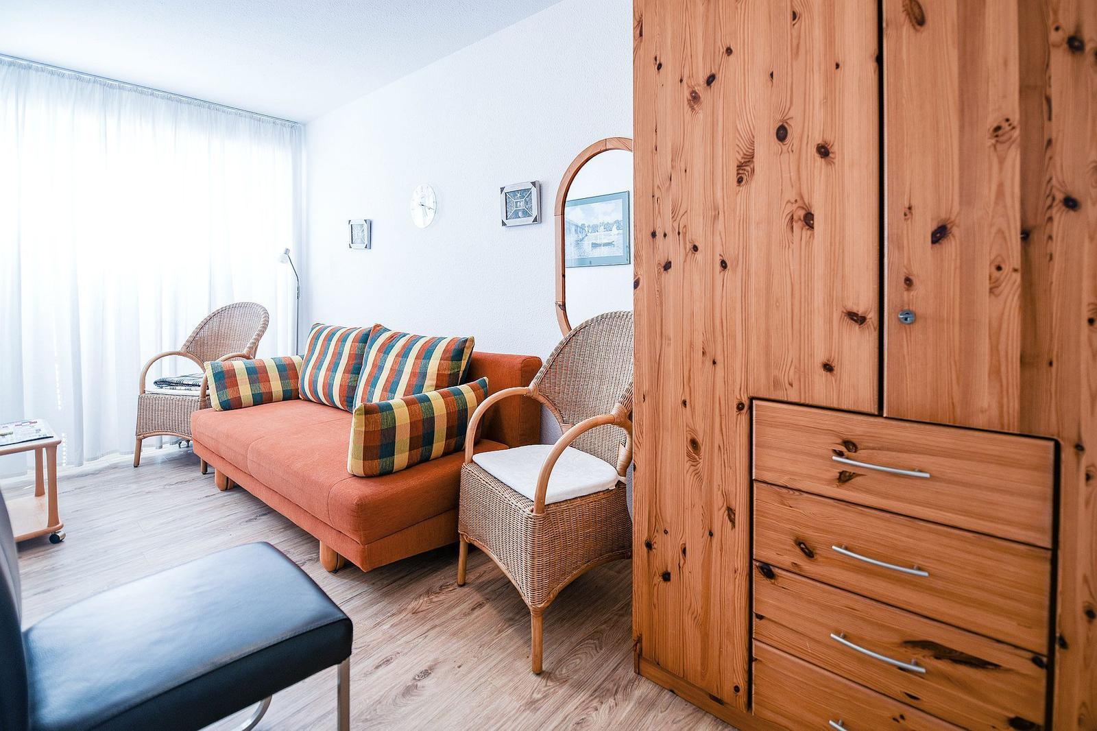 Ein Wohnzimmer mit orangefarbenem Sofa, zwei Rattan-Stühlen und einem Holzschrank.