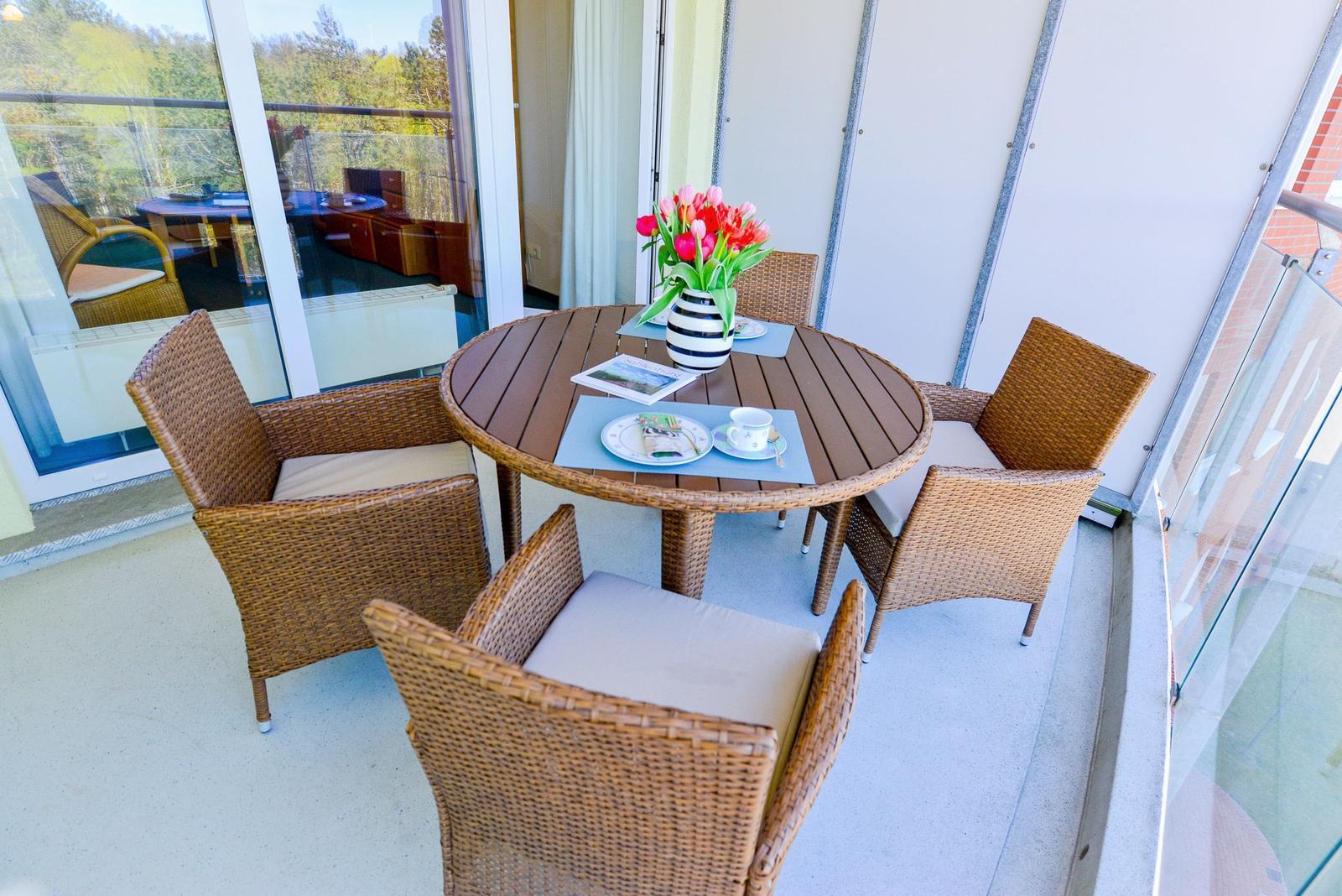 Terrasse mit runden Tisch und vier Stühlen, Blumen und Tischdecken.