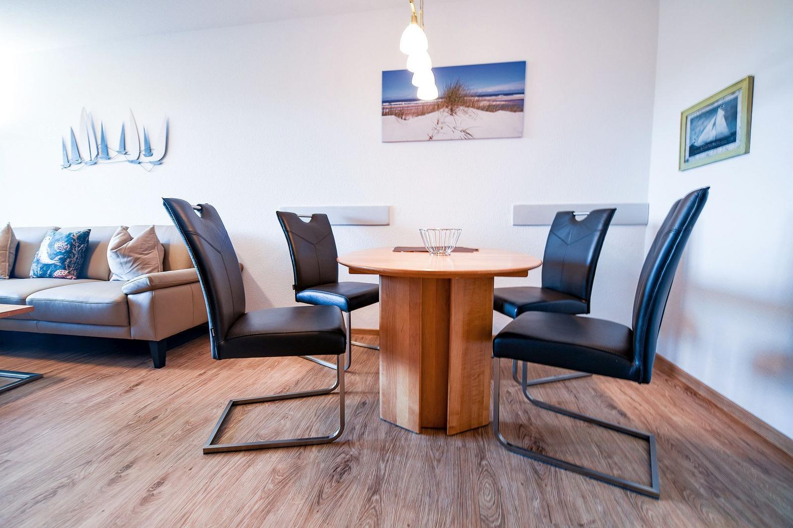 Essbereich mit runden Tisch und vier schwarzen Stühlen. Im Hintergrund Sofa und Wanddekoration.