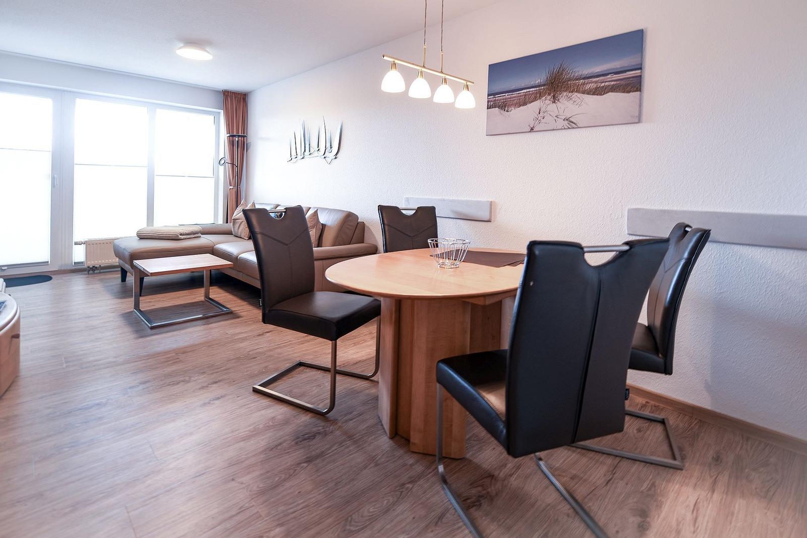 Essbereich mit runden Tisch und schwarzen Stühlen. Wohnbereich mit Sofa und Fenster.